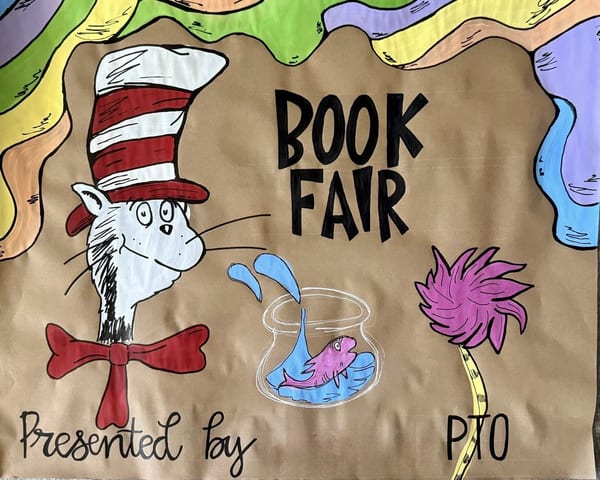 Hand-painted school book fair banner on brown kraft paper with bold black lettering, a striped-hat cat, a fishbowl, a fuzzy pink flower, and a wavy green, yellow, purple, and orange storybook border