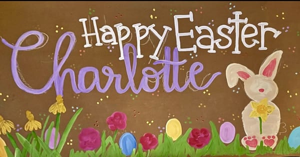 Hand-painted Happy Easter banner on brown kraft paper with white and purple lettering, a cream bunny holding a yellow daffodil, bright flowers, colorful eggs, green grass, and tiny confetti dots for a cheerful spring look